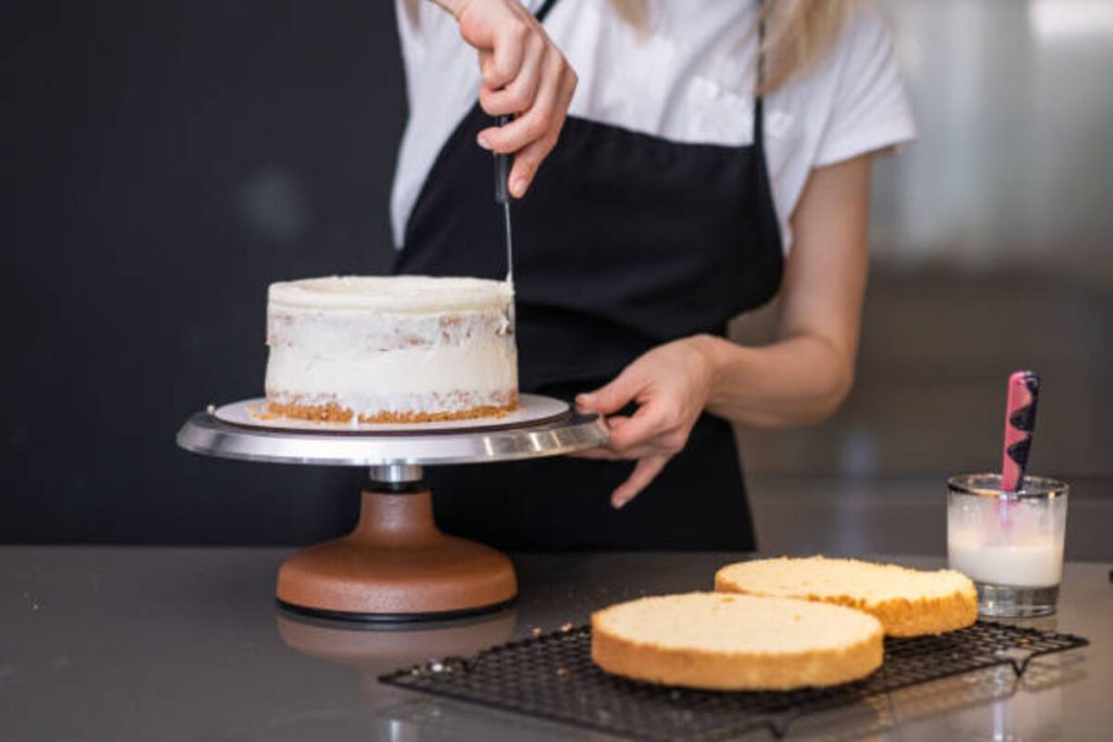 housewife in black apron smearing organic cake layers with fresh white cream in kitchen 1